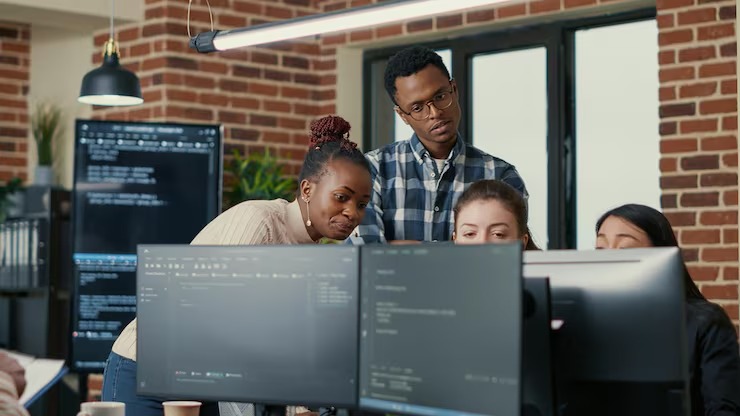 imgi 3 developers brainstorming ideas looking code computer screens asking feedback from senior developer while intern joins discuss